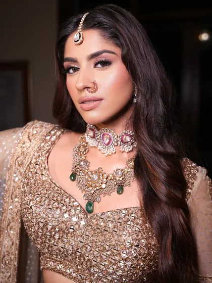 A close-up on the intricate jewelry. The layered choker with emerald and ruby drops adds a pop of color to the monochrome golden look.