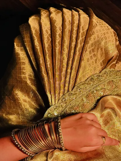 A close-up, artistic shot of the perfectly formed fluffy pleats on a golden Kanchivaram saree. This is my signature technique.