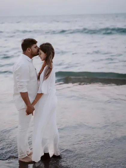 A tender kiss on the forehead as they stand in the gentle waves. This is a classic, timelessly romantic beach photograph.
