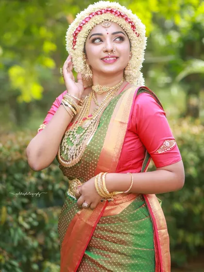 A joyful outdoor portrait of a bride wearing the Sharadha Jalli. The natural light and green background make the traditional attire pop.