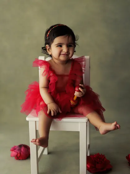 A little girl in a red tutu dress, looking absolutely adorable for her milestone session. The simple background keeps all the attention on her.