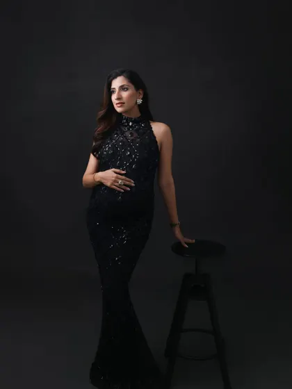 A thoughtful and elegant pose. The dark, minimalist setting allows the sparkling gown and the mom-to-be's quiet confidence to take center stage.