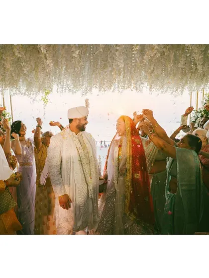 A beautiful, sun-flared shot of the couple during their beachside ceremony, surrounded by celebrating family. This image feels warm, joyful, and cinematic.