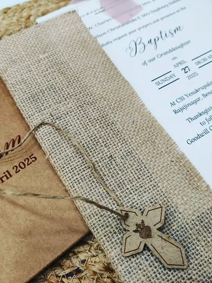 A bespoke Baptism invitation featuring rustic kraft paper, a jute sleeve, and a wooden cross charm for a natural and faith-filled design.