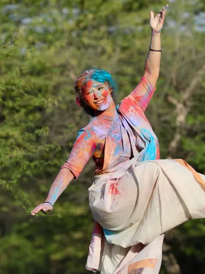 A dynamic, joyful leap captured during a Holi photoshoot. The explosion of organic colors mirrors the vibrant energy of the festival and the dance.