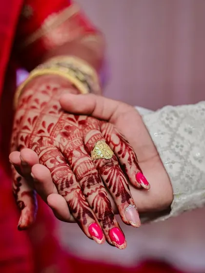 A detailed close-up shot of the bride's hand, adorned with henna and the engagement ring, held by the groom.