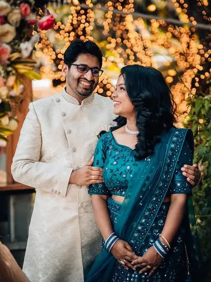 A classic reception portrait of a couple, smiling at each other in front of a beautiful floral and light-filled backdrop.