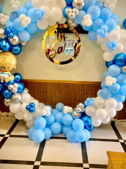 An "Oh Baby" themed decoration perfect for a baby shower or a baby's first birthday. This circular balloon arch in shades of blue and white is accented with chrome silver and a cute baby boy foil balloon.