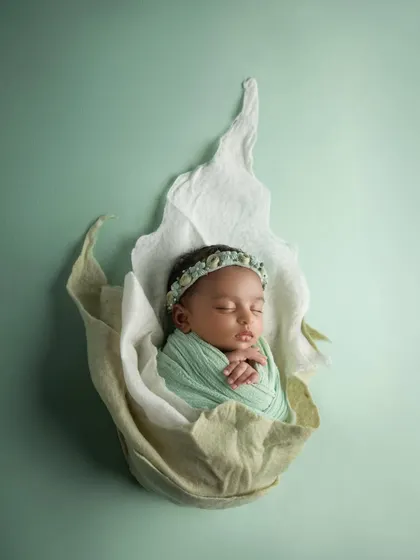 A newborn girl wrapped in a soft mint green swaddle, nestled inside a white and green flower prop. This creates a fresh, organic, and ethereal portrait.