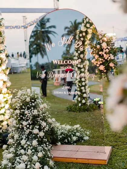 A personalized welcome sign on a mirror, reflecting the beautiful floral decor and palm trees of the Goa venue.