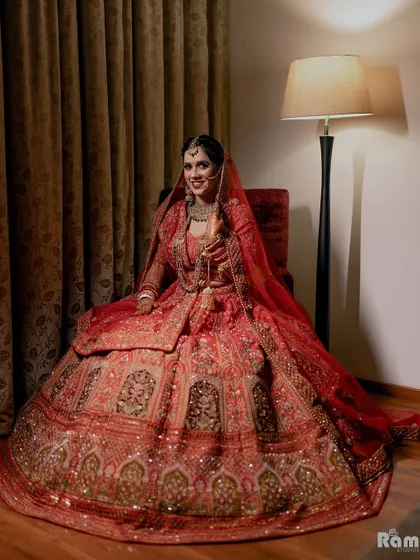 A beautiful portrait of the bride seated in her grand red lehenga, looking happy and radiant on her wedding day.
