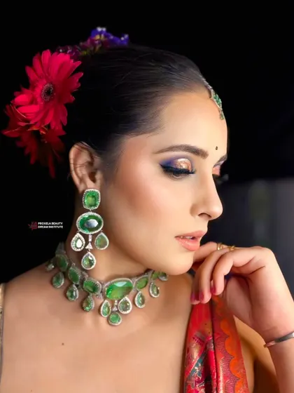 Grace in every glance. This elegant look features a pop of blue under the eye, beautifully complementing the emerald green jewelry and red outfit.