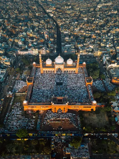 A high-altitude perspective of Jama Masjid, showing the main road leading to the mosque filled with people. This shot emphasizes the sheer volume of attendees and the grandeur of the location during the Eid festival.