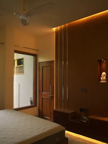 This bedroom interior uses warm lighting and wood paneling to create a cozy and inviting atmosphere. The design includes a niche for placing small artifacts, adding a personal touch to the space.