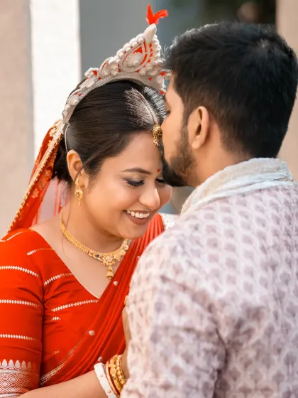 A close-up, intimate moment from a Bengali wedding, the groom placing a loving kiss on the bride's forehead.