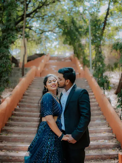 A romantic kiss on the cheek, framed by a grand staircase during a pre-wedding shoot.