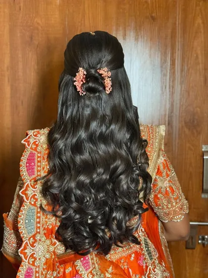This half-updo features a small bun made of twists, with the rest of the hair styled in defined waves. The delicate pink floral clips add a romantic touch.