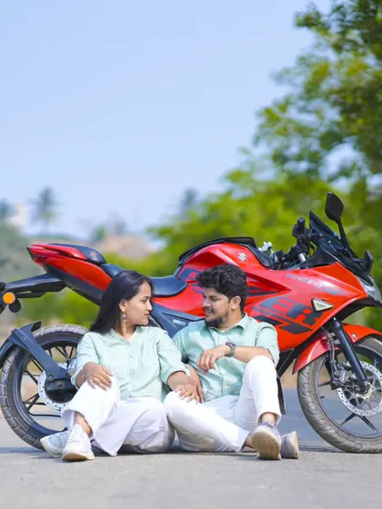 A relaxed and romantic photo of a couple sitting by their motorcycle on an open road.