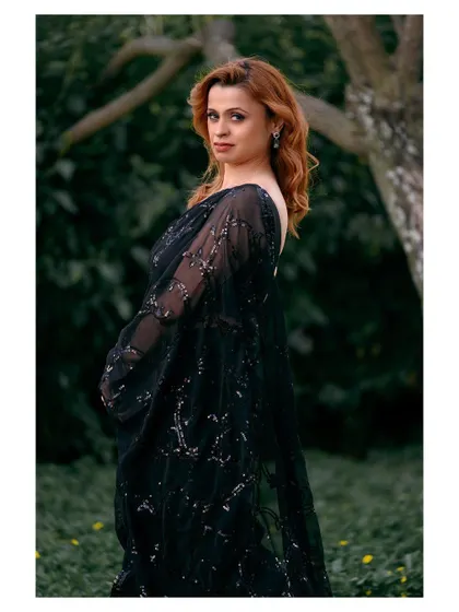 An outdoor portrait in a black sequined saree. The natural green background provides a beautiful contrast to the glamorous outfit.
