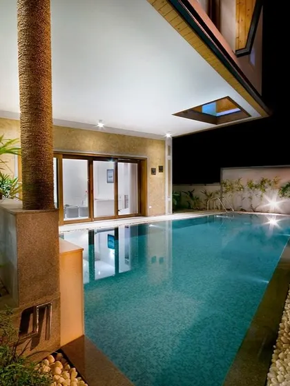 A covered poolside lounge designed for evening relaxation. The combination of warm interior lighting, underwater pool lights, and a skylight creates a magical ambiance after dark.