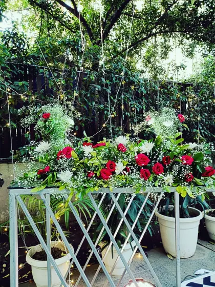 A lush floral arrangement of red and white roses with baby's breath, set against a backdrop of greenery and fairy lights.