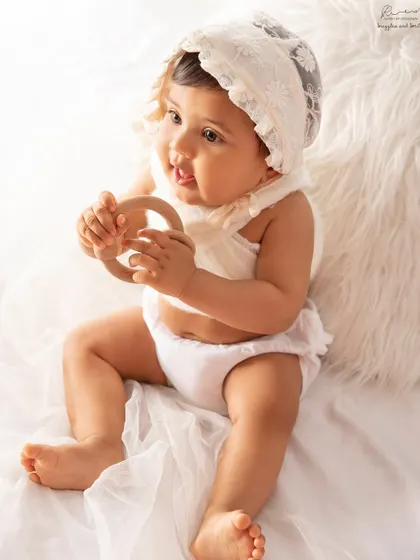 An all-white setup for a classic and pure baby portrait. This little one is exploring a wooden teether, completely in her own world.