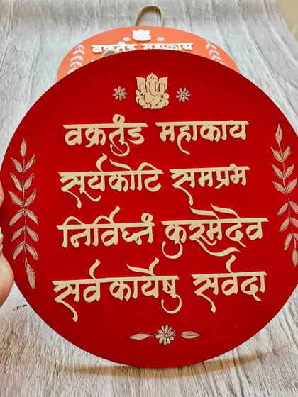 A closer look at the red 'Vakratunda Mahakaya' wall hanging, showing the 3D lettering and hand-painted details.