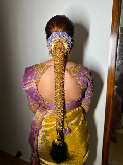 This is a stunning example of a traditional bridal braid adorned with heavy gold jewellery. The combination of the lavender-hued flowers and the gold saree creates a breathtaking look.