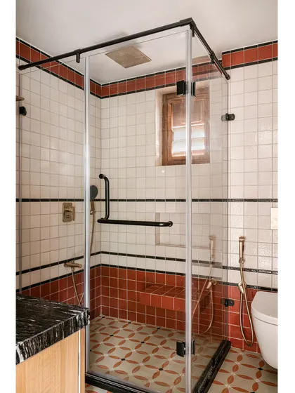 A view of the glass-enclosed shower, showing the built-in tiled bench and the warm brass fixtures.