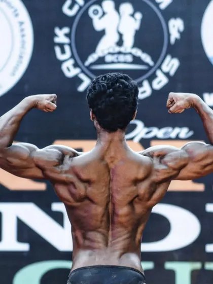A back double biceps pose on stage. This is a clear example of the results of a focused back and shoulder workout regimen.