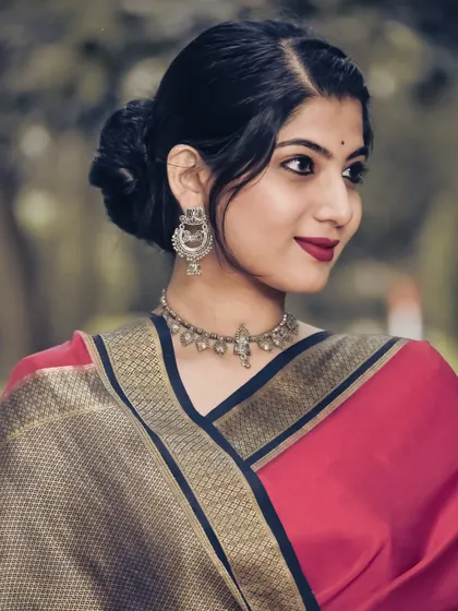 A classic portrait in a pink and black saree, with a focus on the elegant drape and traditional silver jewelry. The soft smile and confident pose create a timeless appeal.