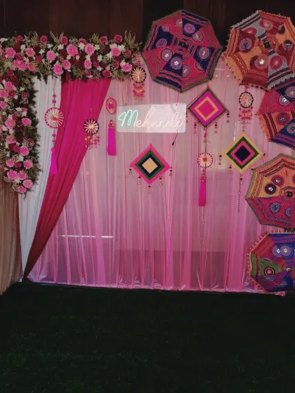 A beautiful Mehendi backdrop with a pink and white theme. I used an L-shaped floral arch, traditional embroidered umbrellas, and a 'Mehendi' neon sign for a festive look.