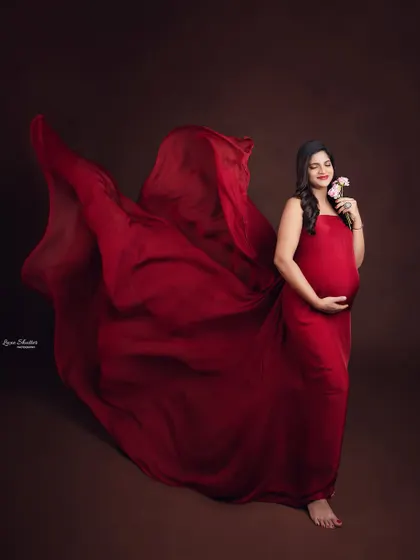 A serene moment with the mom-to-be holding delicate flowers, her red gown flowing gracefully behind her.