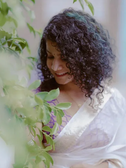 A candid and sweet moment during an Onam-themed shoot. The way she interacts with the leaves, combined with her beautiful curly hair and traditional saree, creates a soft and natural portrait.