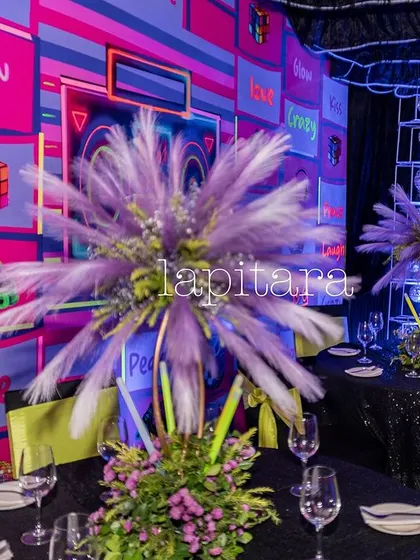 A table setting at the neon party, featuring a large feathery centerpiece and a backdrop of glowing, colorful panels.