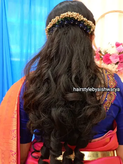Soft, natural waves for a traditional look. This half-up style is adorned with a floral accessory that complements the client's saree.