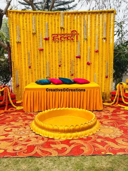A clean, bright shot of the classic Haldi decoration. The vibrant yellow marigold wall is the perfect backdrop for this joyous occasion.