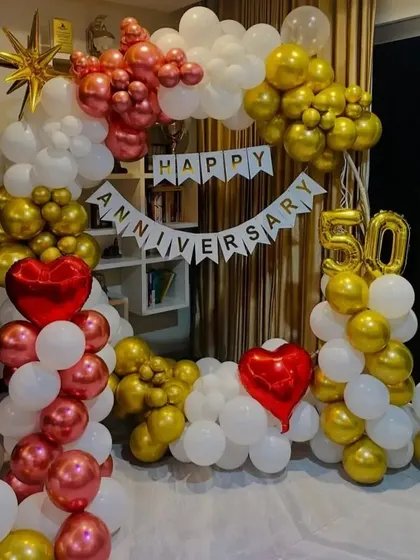A festive 50th anniversary celebration setup indoors. I created a full balloon arch using a classic combination of red, gold, and white balloons, complemented by a 'Happy Anniversary' banner and large '50' foil numbers.