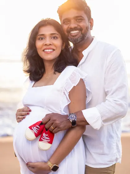 A joyful portrait of the couple, holding up a pair of bright red baby shoes, a fun and colorful way to announce their excitement.