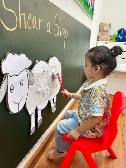 A fun and messy way to learn. This child enjoys the tactile sensation of "shearing" the fluffy wool, combining sensory play with thematic learning about farm life.