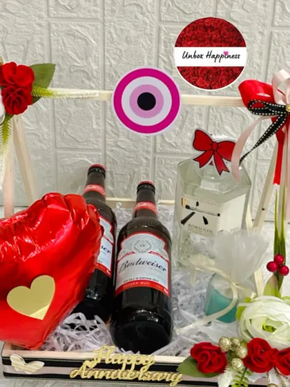 A close-up of the anniversary basket, showing the arrangement of drinks, an evil eye charm, and decorative flowers.