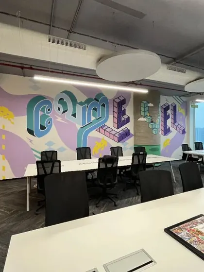 A large meeting area in the Kissflow office with a custom graffiti-style mural. The exposed ceiling and industrial lighting are balanced by the colorful artwork, creating a space that is both raw and creative.