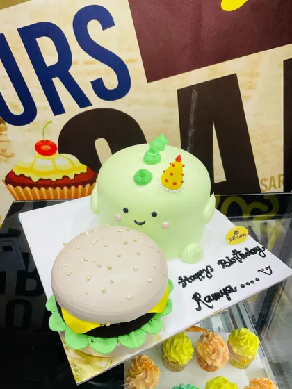 A playful 3kg set featuring two cakes: one shaped like a hamburger and the other like a cute green dinosaur.