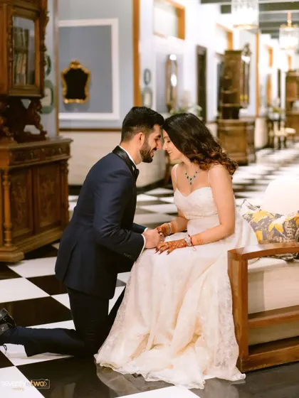 The groom on one knee before his bride on a classic checkered floor, a timeless romantic gesture captured in the elegant interiors of the Mayfair Siliguri.