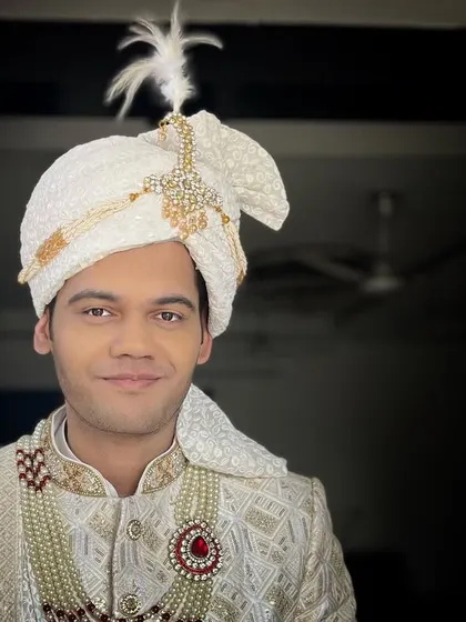 A portrait of a groom ready for his wedding. His look features a white textured sherwani, a matching safa with a 'kalgi', and a stunning ruby brooch, all tied together with my expert grooming.