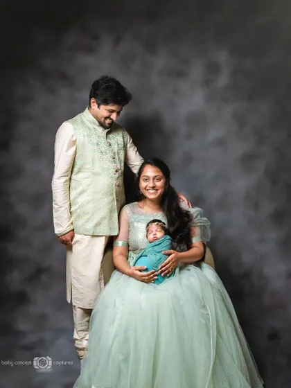 A formal family portrait with the parents dressed in elegant traditional wear, smiling down at their newborn. We can style your family session to match your vision.
