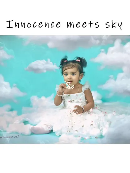 A dreamy and innocent portrait of a baby girl sitting among fluffy white clouds against a sky-blue background, creating a magical, heavenly scene.