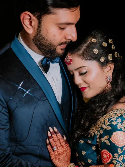 A tender close-up of the couple, showcasing the bride's intricate henna and the groom's stylish blue tuxedo.