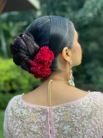 Another angle of the high bun with coxcomb flowers, showing the beautiful contrast against the bride's pastel pink lehenga.