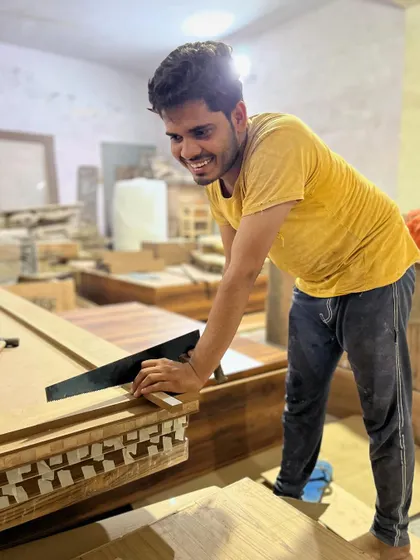 Precision in progress. Here, one of our craftsmen is working on the intricate details of a furniture piece, ensuring every joint and finish meets our high standards of quality.